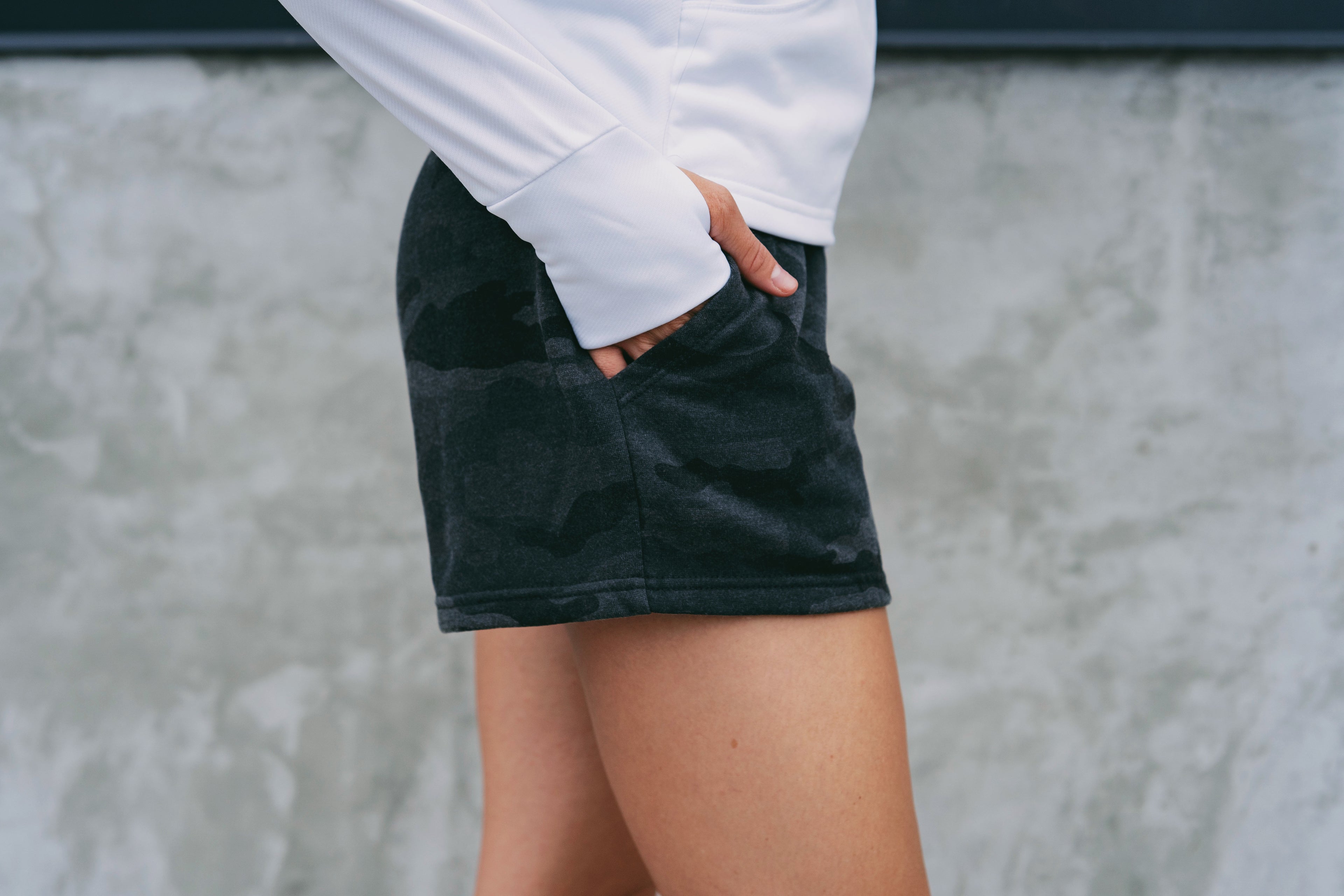 Person wearing a black skirt and white long-sleeve shirt against a gray wall.