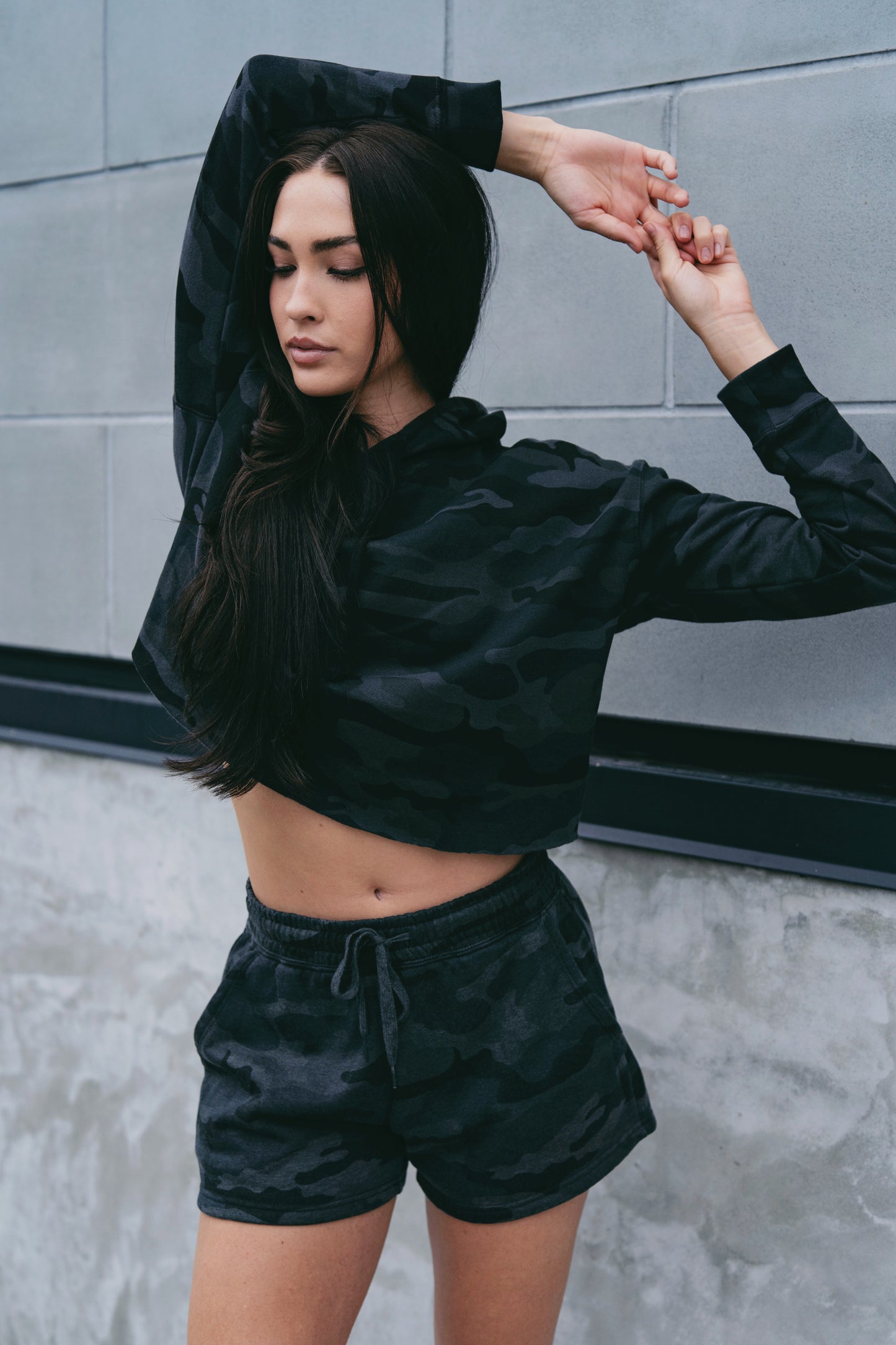 Woman wearing a black satin outfit against a gray wall.