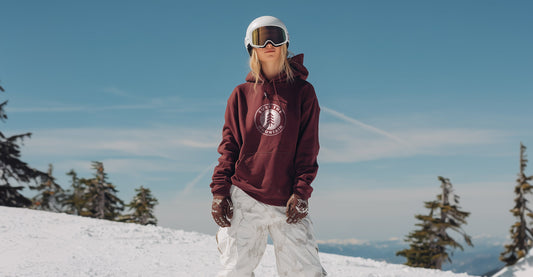 Person snowboarding on a snowy slope with a clear blue sky and trees in the background