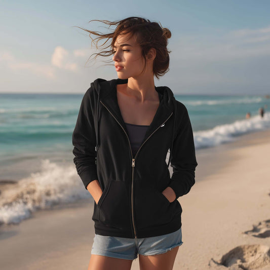 Woman in black hoodie and denim shorts standing on a beach with ocean waves in the background