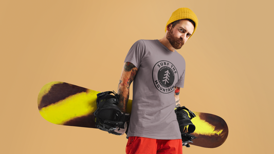Man holding a snowboard wearing a surf the mountain barbwire beach graphic t-shirt