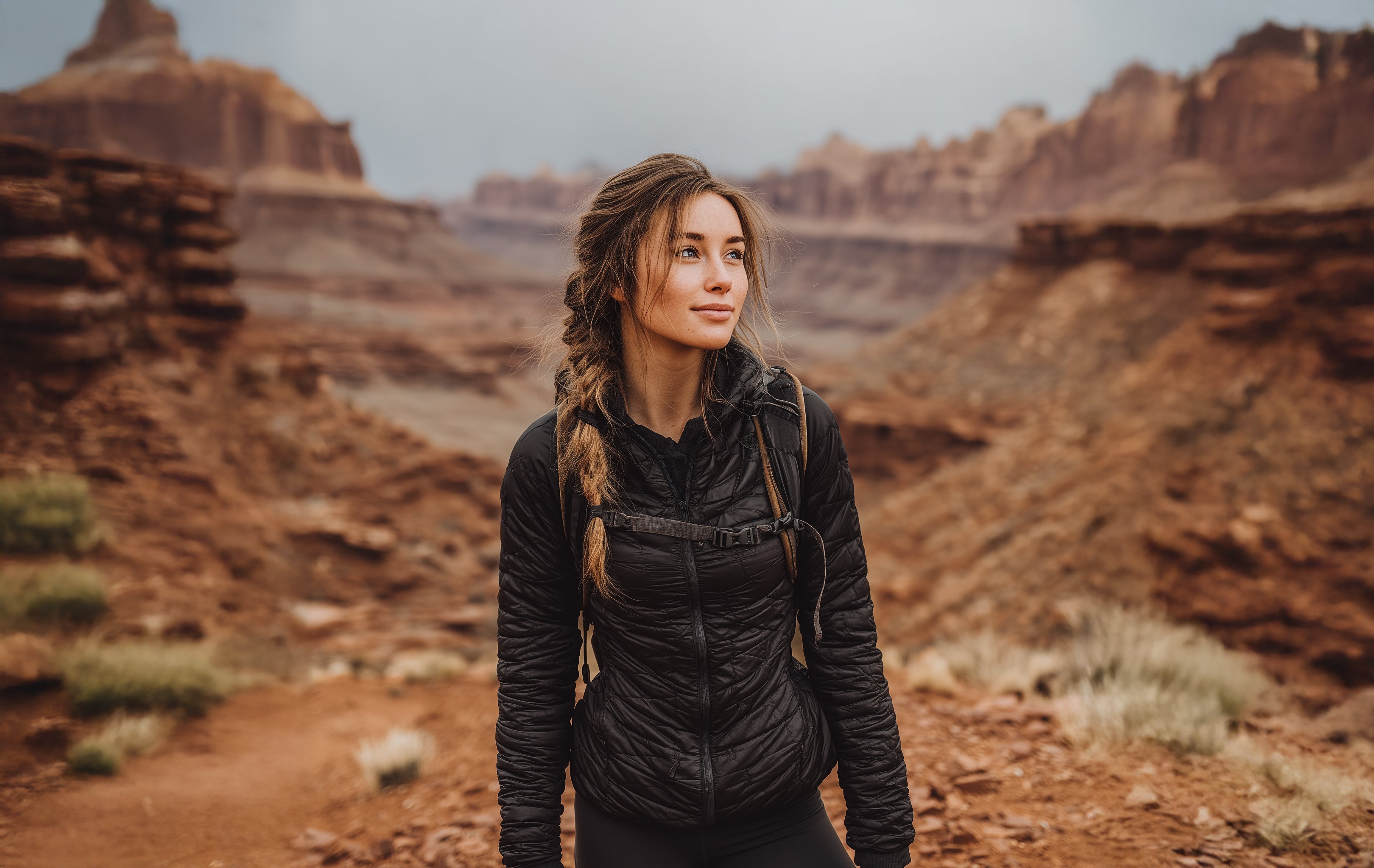 Woman in a black jacket standing in a desert landscape with red rock formations.