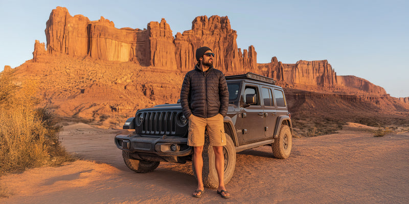 Man standing next to a Jeep in a desert landscape with rock formations.