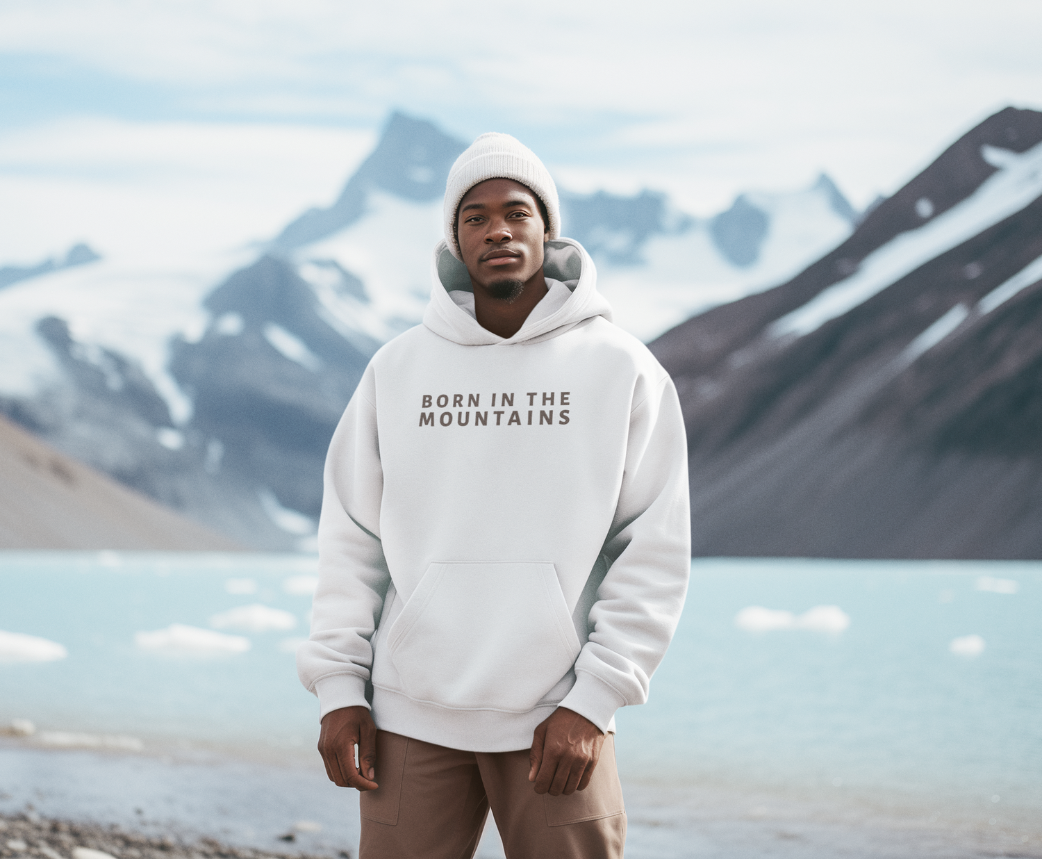 Person wearing a hoodie with 'Born in the Mountains' text in front of a mountainous landscape.