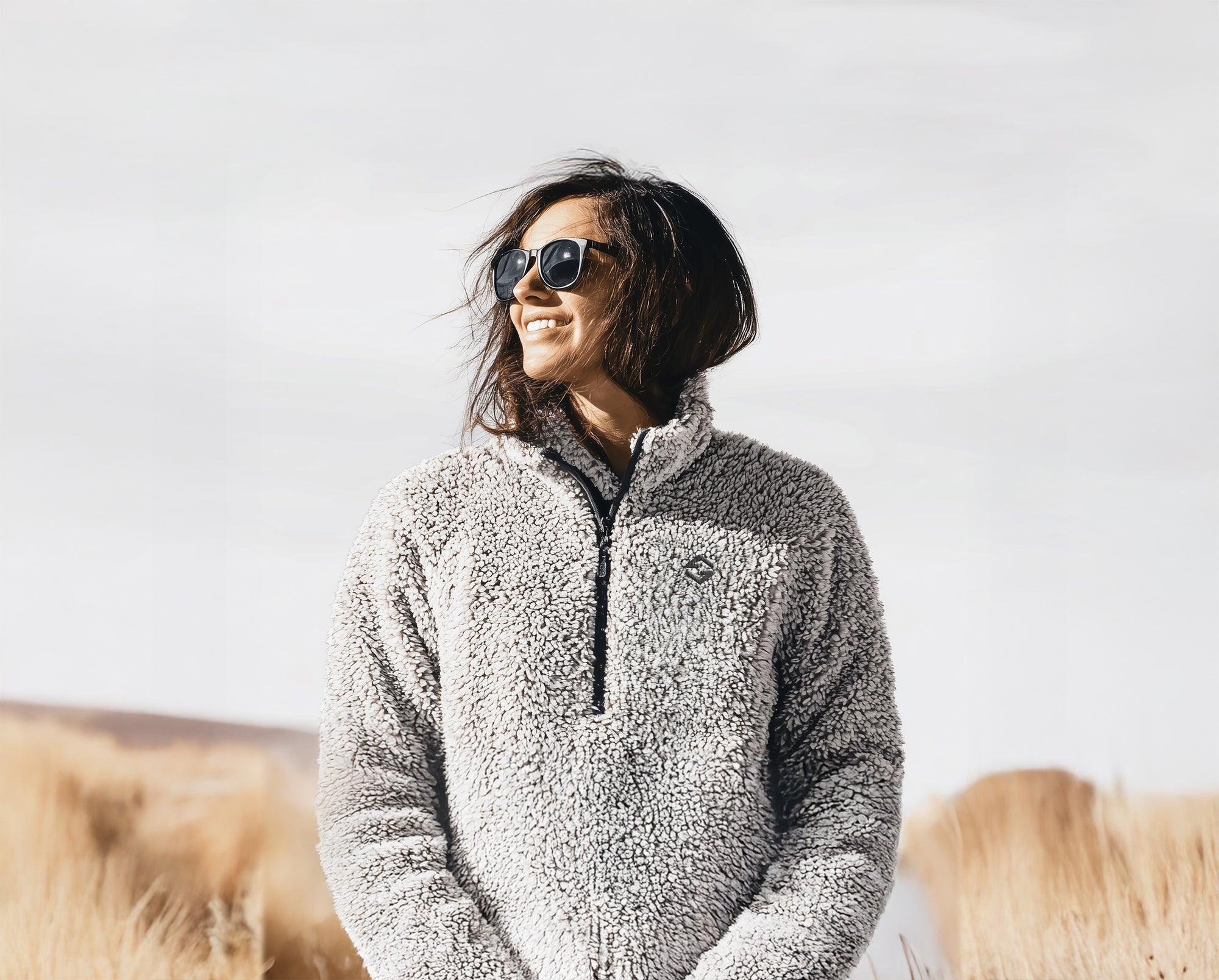 Person wearing a gray fleece jacket with sunglasses against a plain background