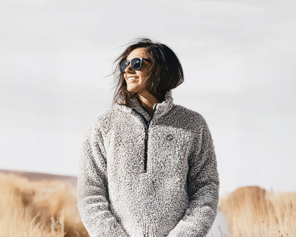Person wearing a gray fleece jacket with sunglasses against a plain background